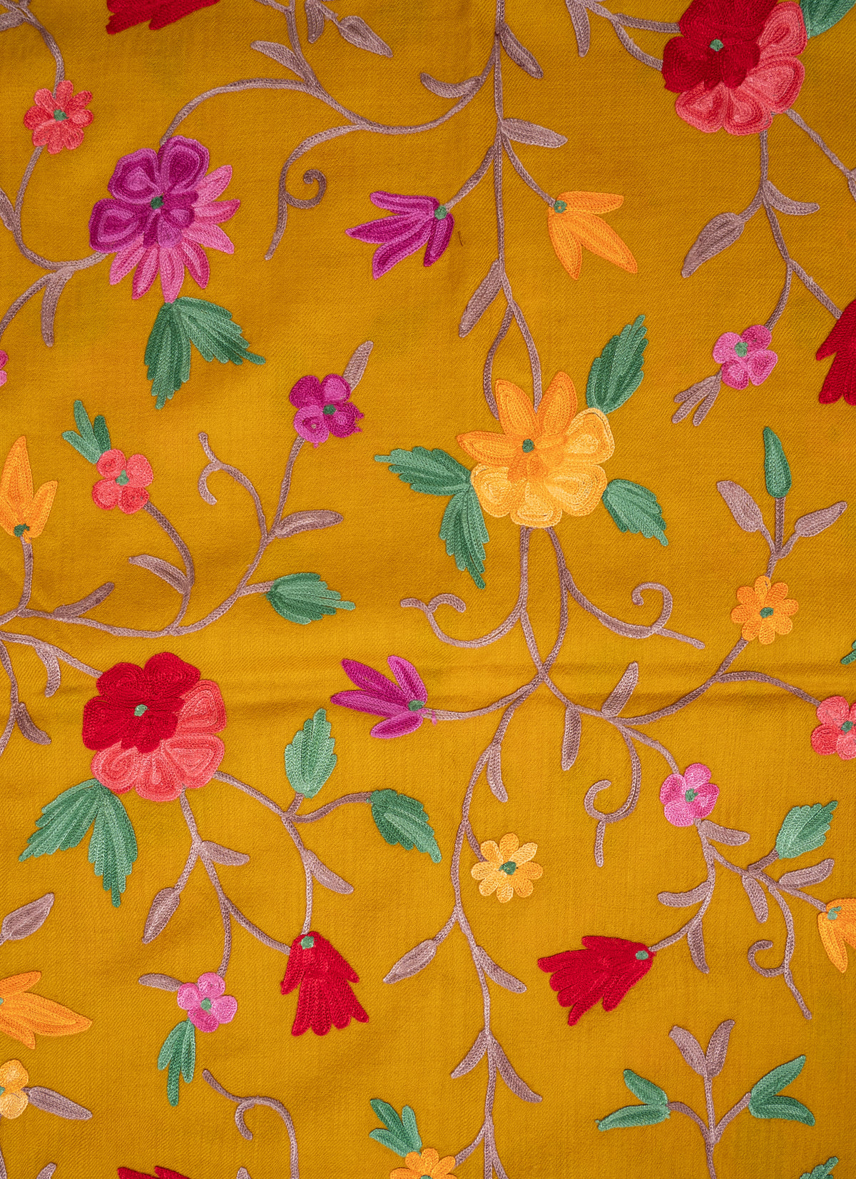 Close-up of red, pink, purple and yellow Aari flowers with green leaves and pale stems on mustard shawl