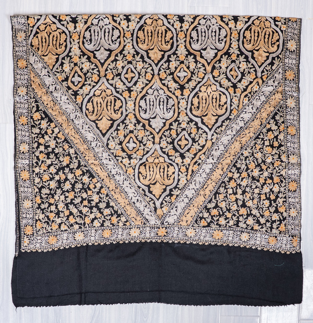 Black shawl spread flat, with ivory and gold-toned Aari medallions in a V-shaped panel above a plain black end