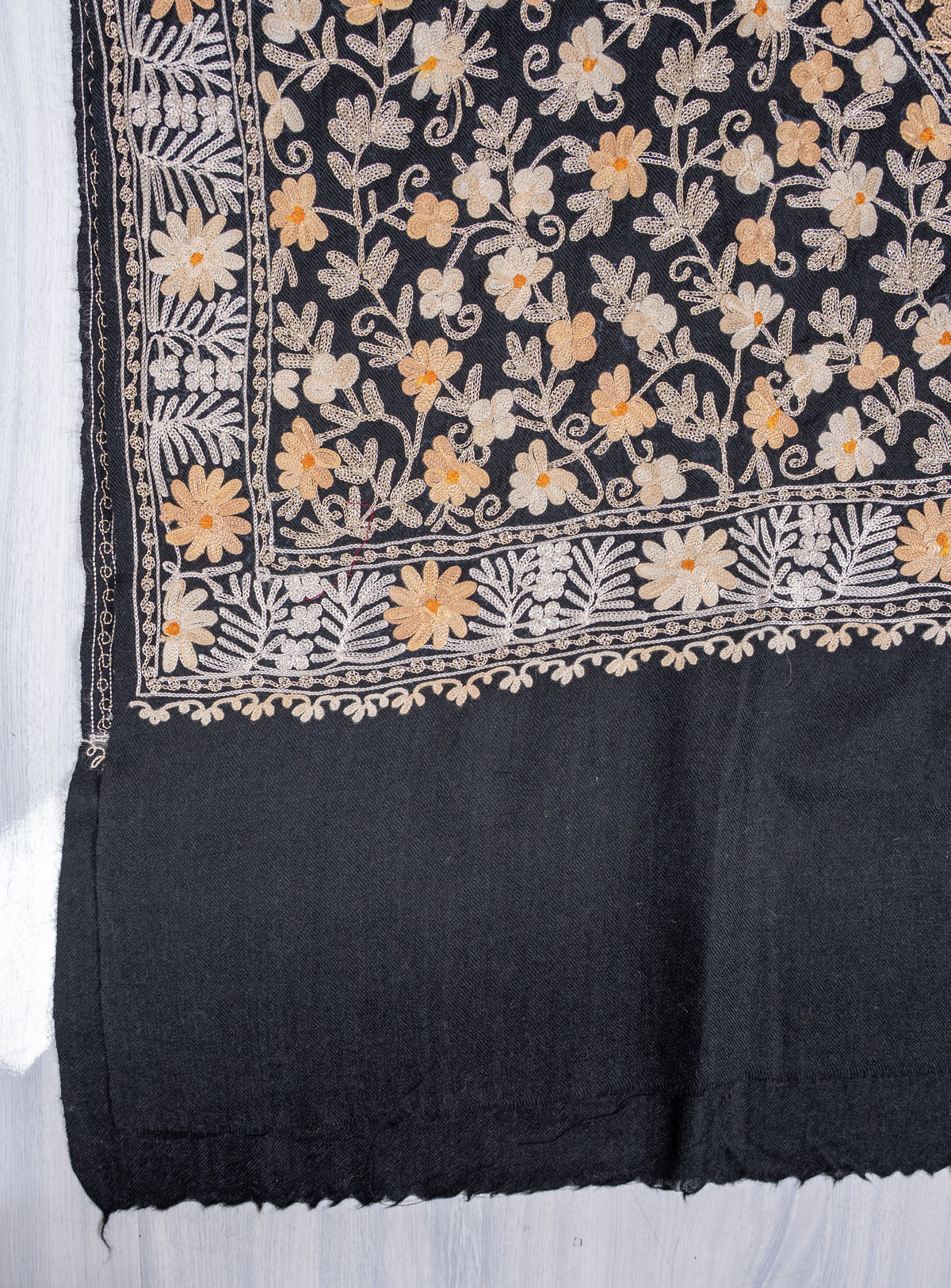 Flat corner detail of the black shawl, with ivory and gold-toned Aari floral vines and layered borders above a plain end