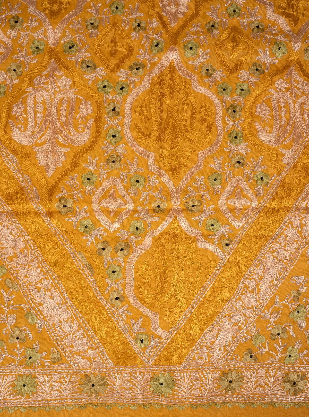 Close-up of the mustard shawl’s pale and tonal Aari medallions, framed by small flowers and diagonal embroidered bands