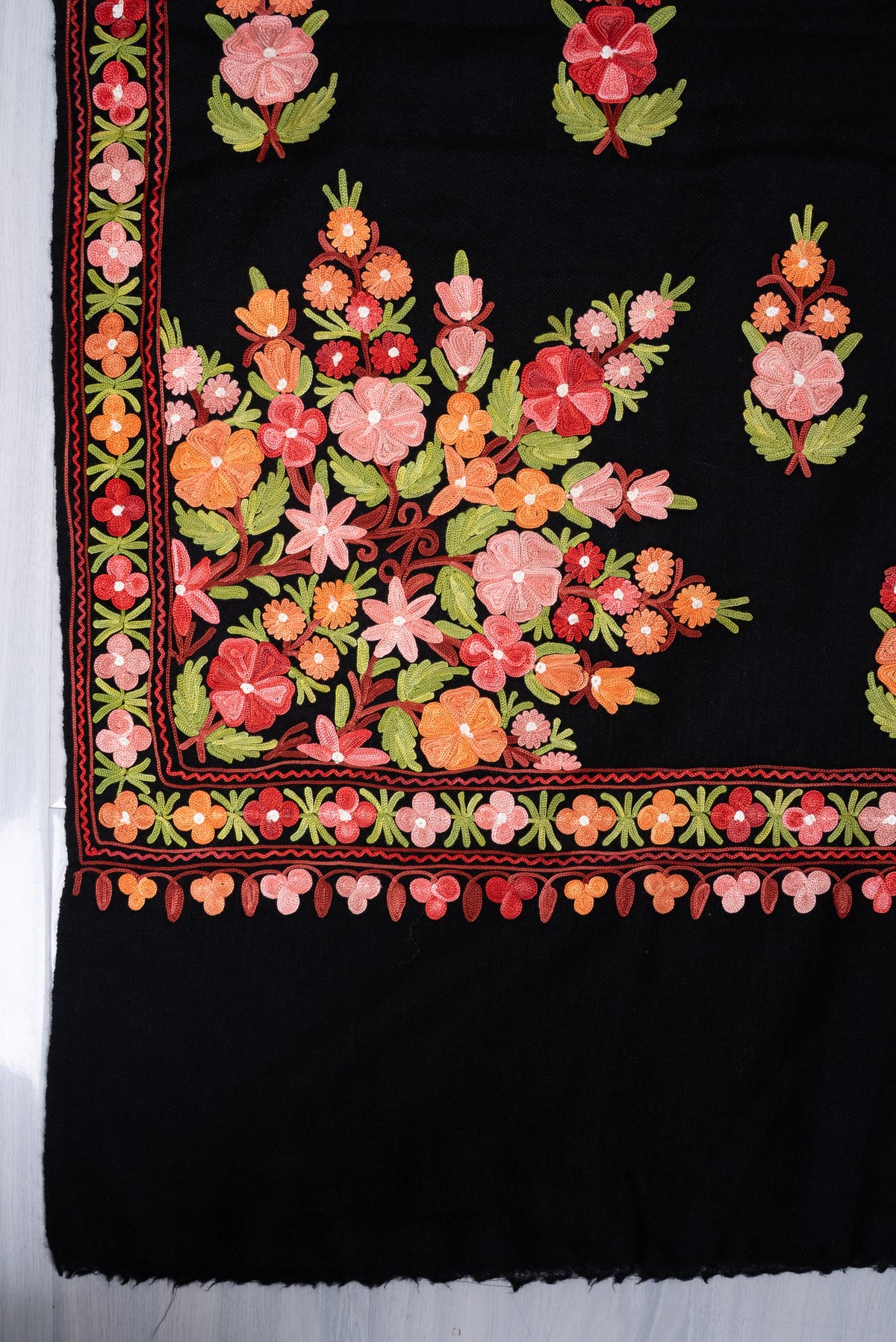 Corner of black shawl showing a large pink, orange and red floral bouquet, narrow borders and a plain black end