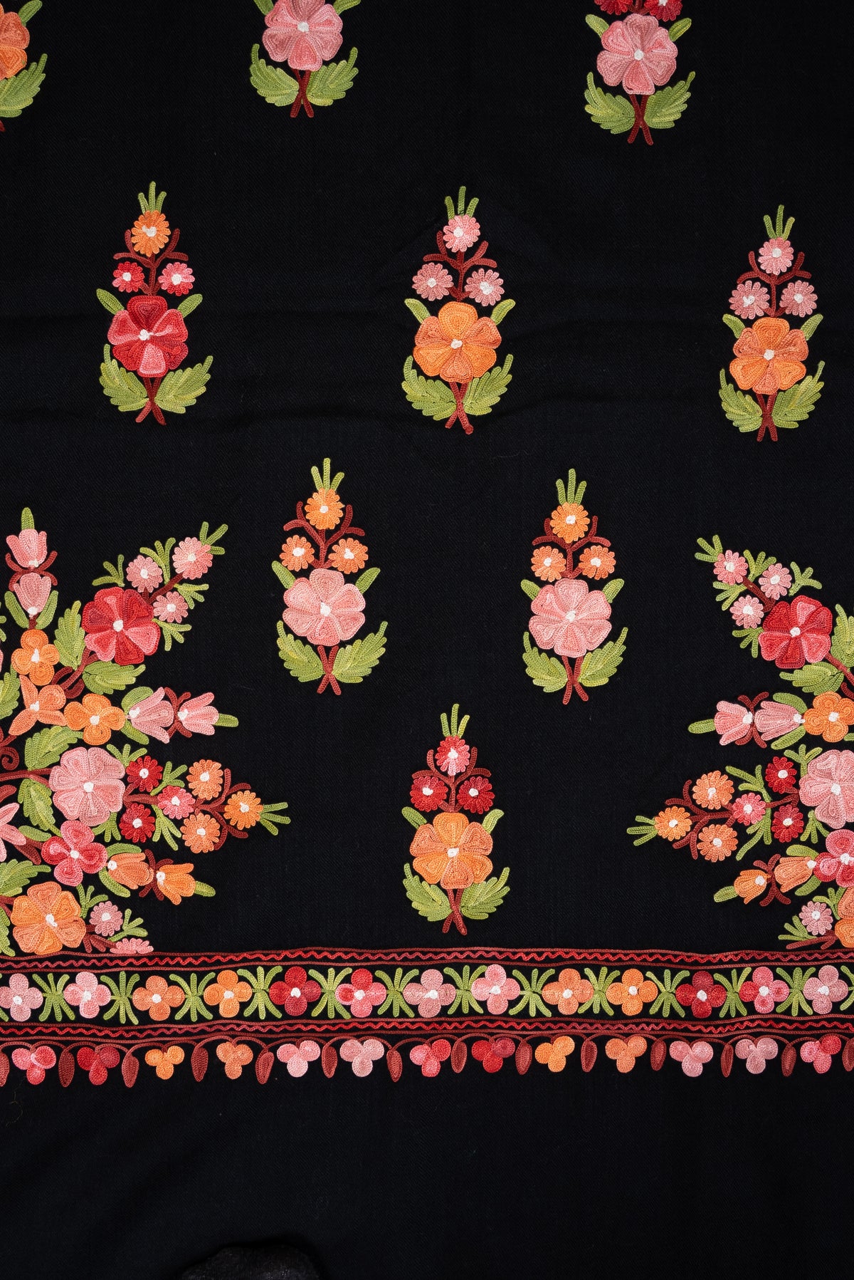 Black shawl detail showing rows of colourful floral sprigs and large corner bouquets above the embroidered end border