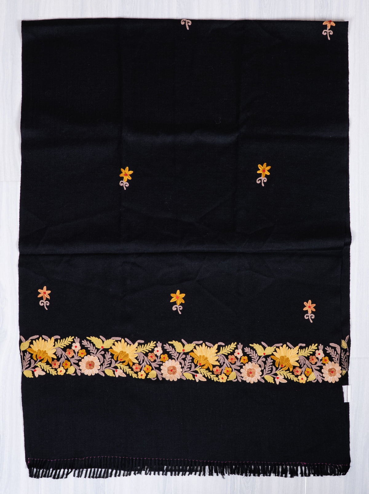 Black shawl spread flat, with scattered yellow Aari flower sprigs and a cream and yellow border above a fringed end