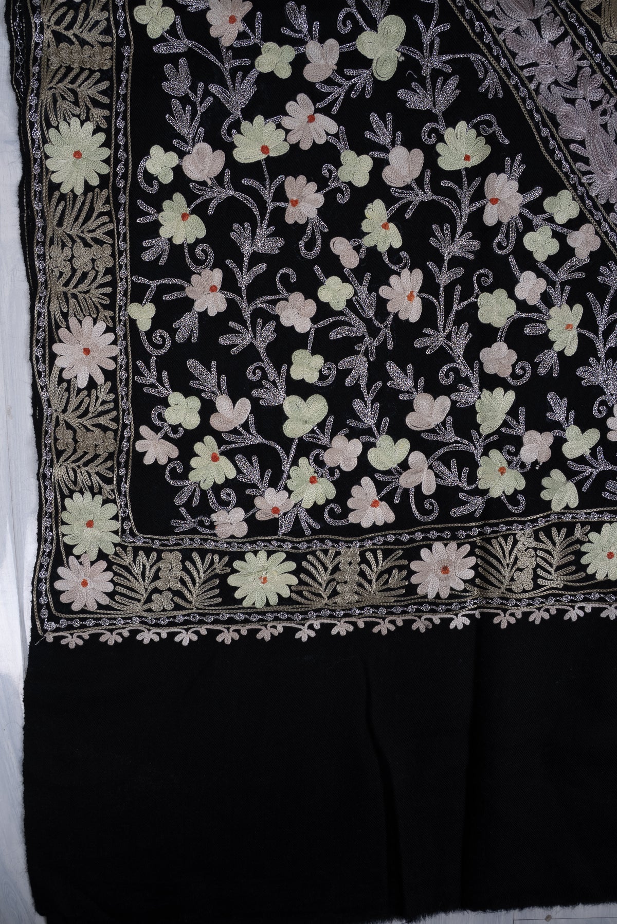 Flat corner detail of the black shawl, with pale Aari flowers on curling stems and layered borders above the plain end