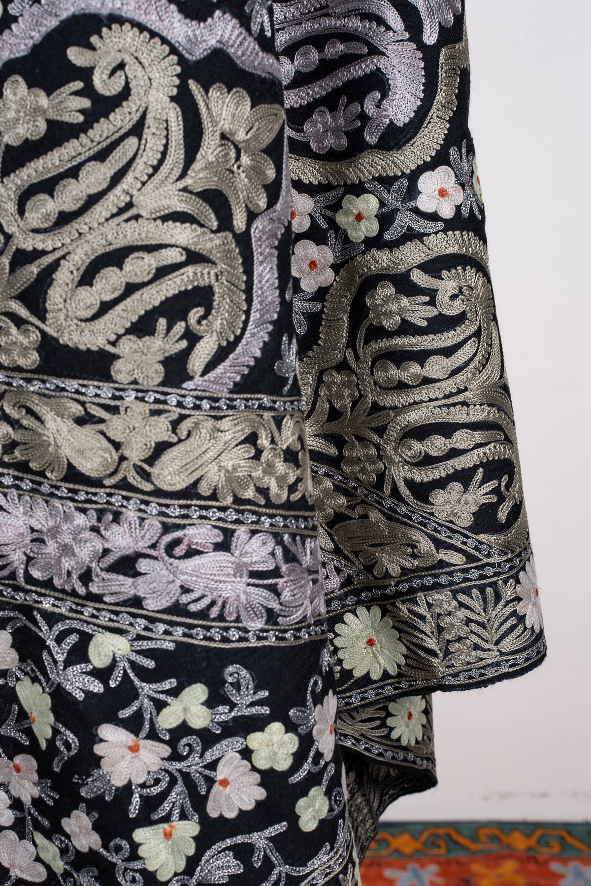 Lower draped detail of the black shawl, showing pale Aari medallions, small flowers and layered floral borders