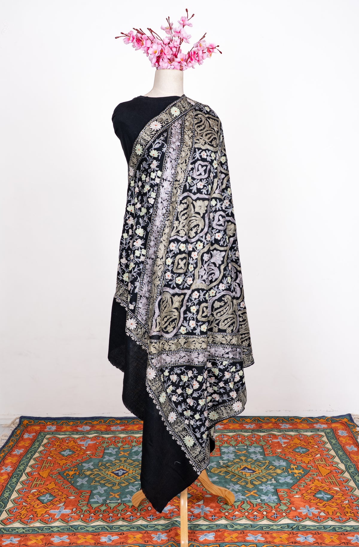 Full view of the black shawl on a mannequin, with pale Aari medallion panels, floral borders and a plain black end