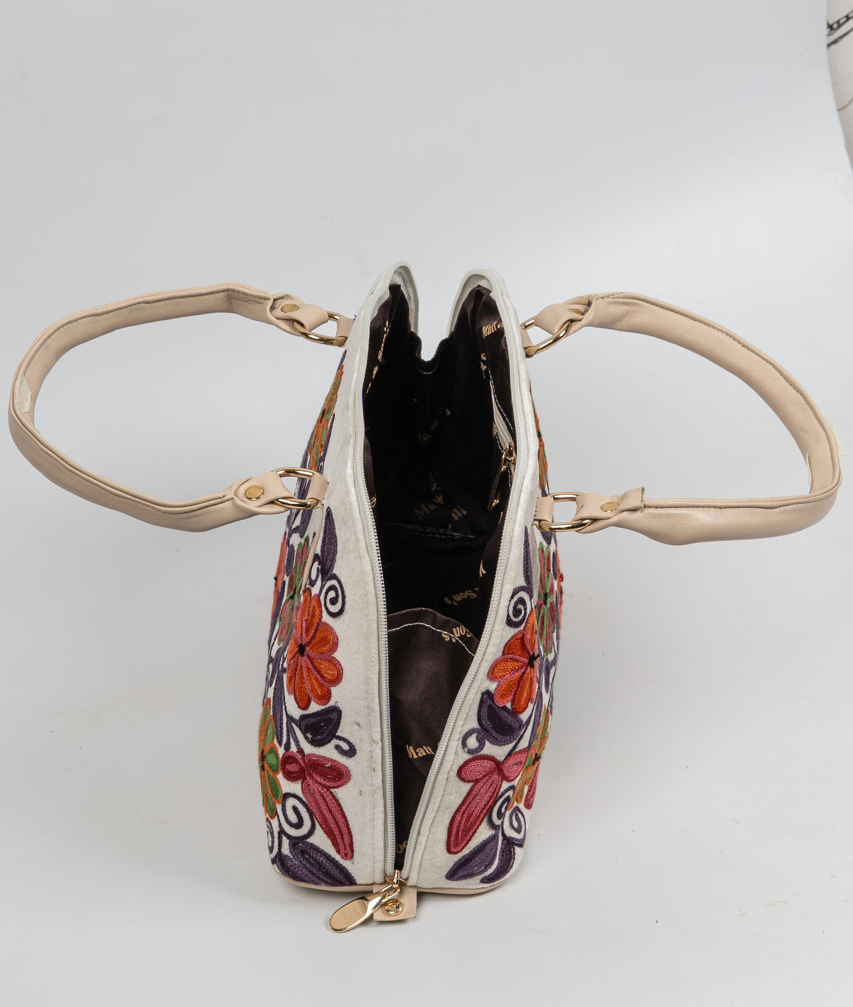 Top view of an open ivory floral Aari tote with dark lining, cream handles spread outward and gold-toned fittings