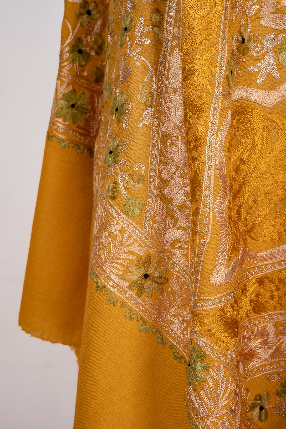 Lower draped detail of the mustard shawl, showing pale Aari floral bands and tonal paisleys beside the plain end