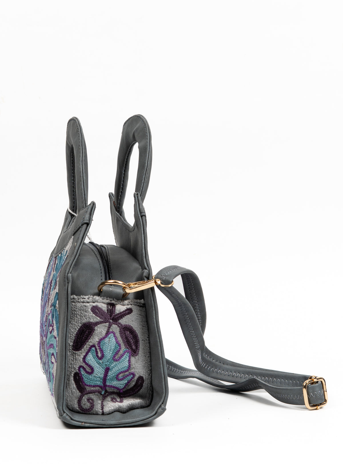Side view of the grey handbag with an embroidered leaf panel, metal strap clip and adjustable grey shoulder strap.