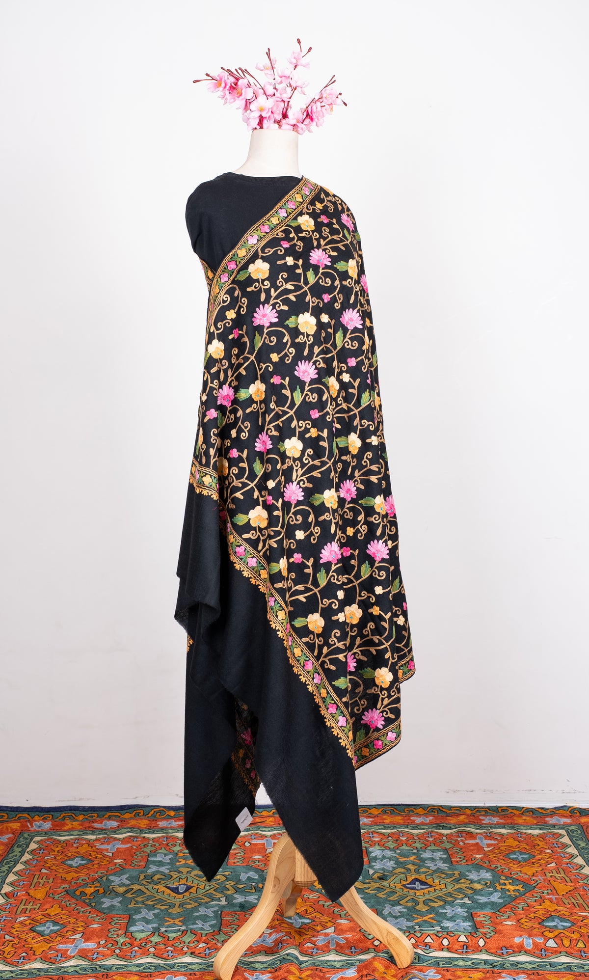 Black shawl draped on a mannequin, with pink and cream Aari flowers on curling tan vines, a floral border and plain black ends.