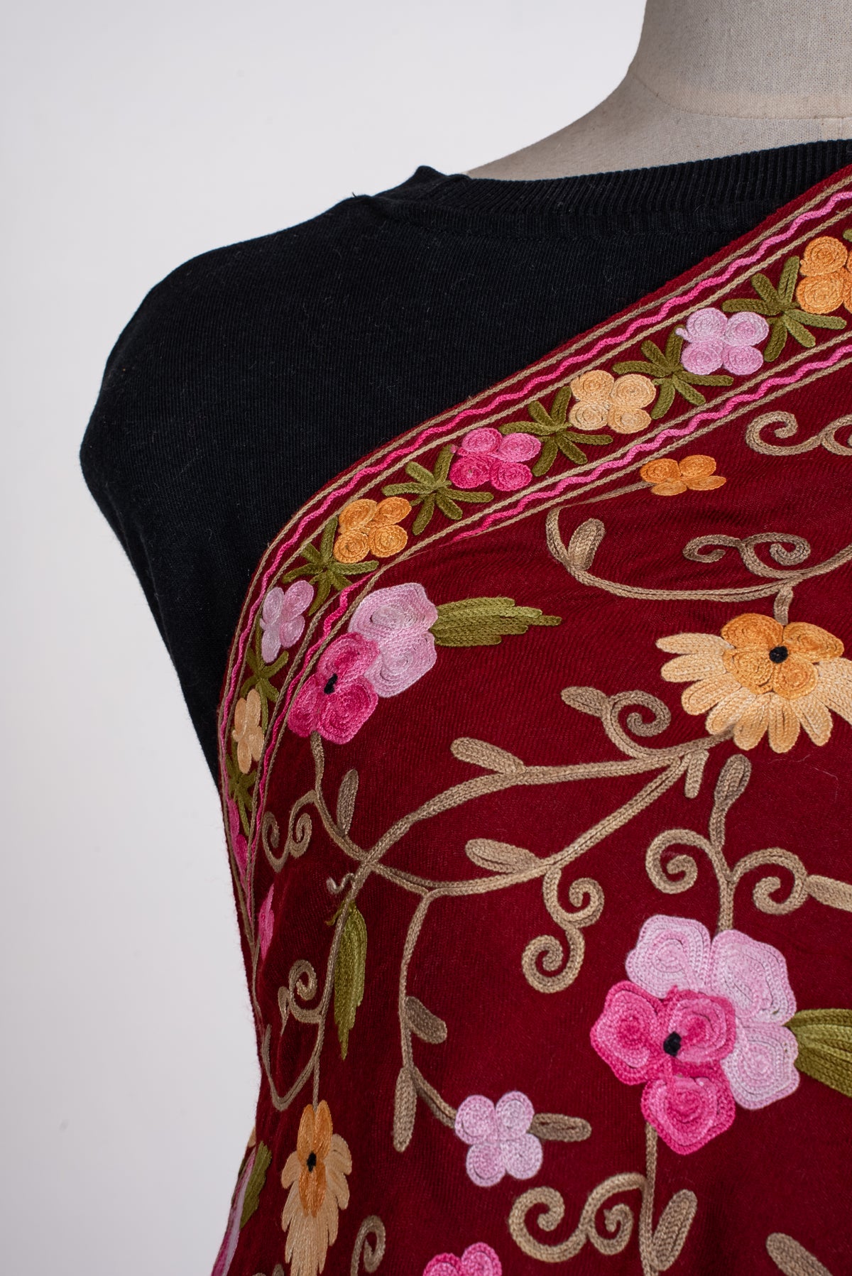 Shoulder close-up of maroon shawl showing pink and golden floral Aari vines beside the matching embroidered border