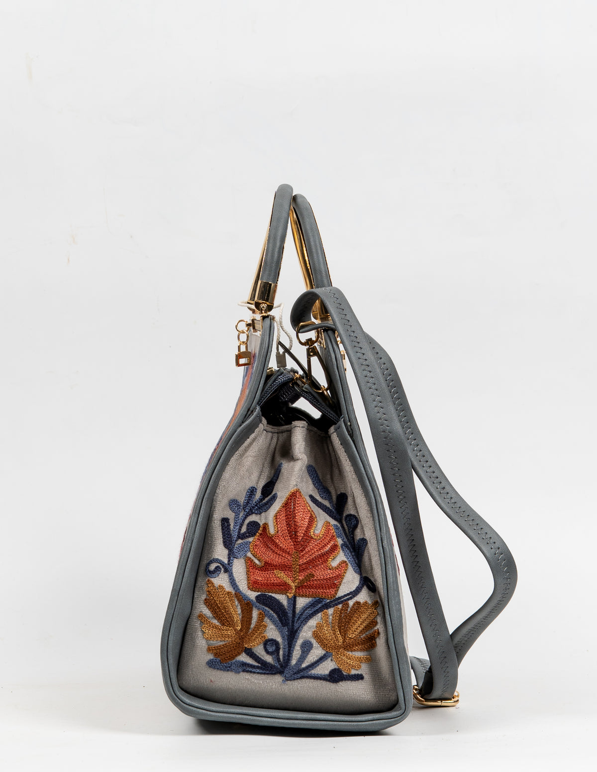 Side view of the beige handbag with a large orange leaf motif, blue stems, grey edging and a shoulder strap