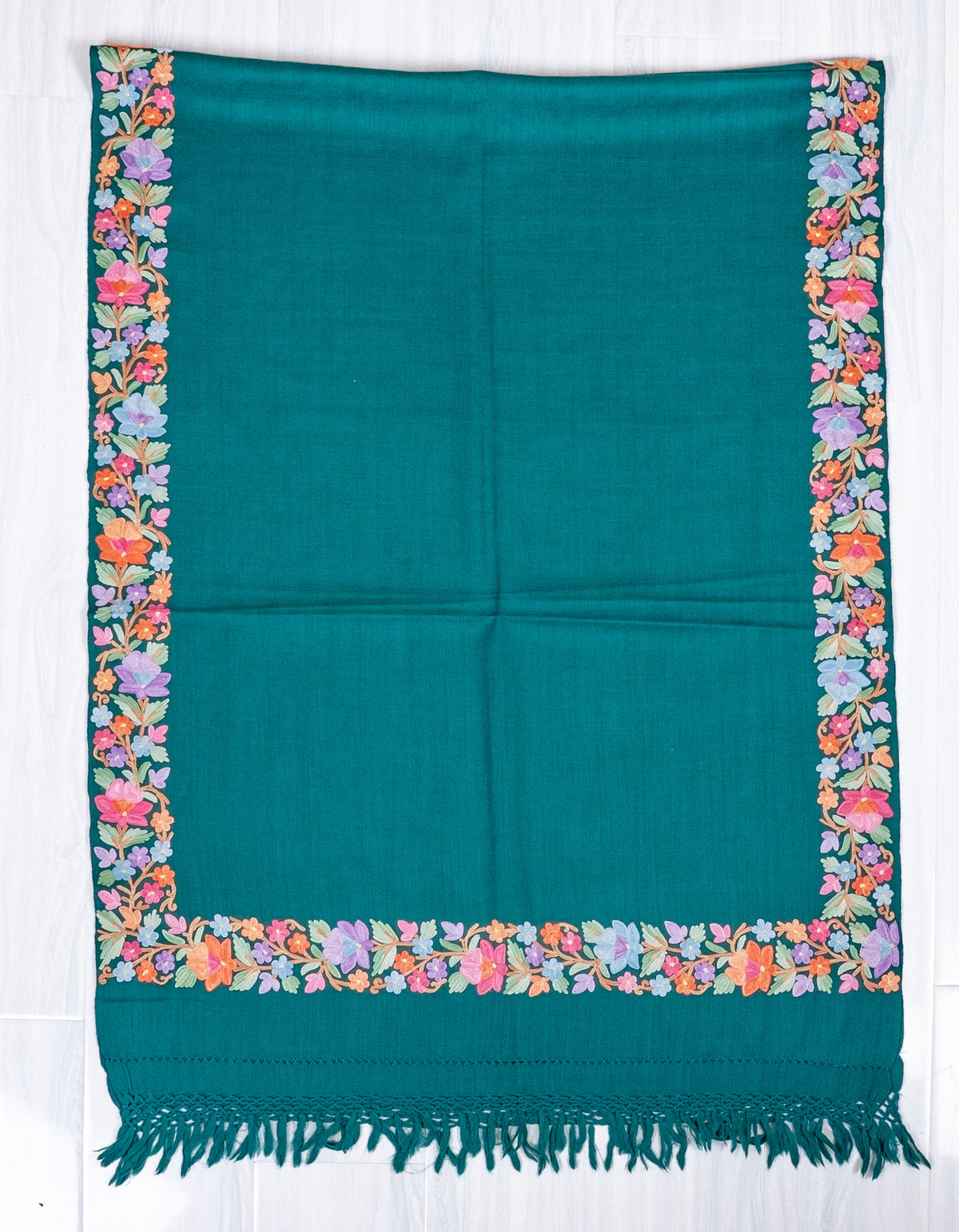 Teal shawl laid flat lengthwise, with a plain centre framed by pastel Aari floral borders above matching knotted fringe.