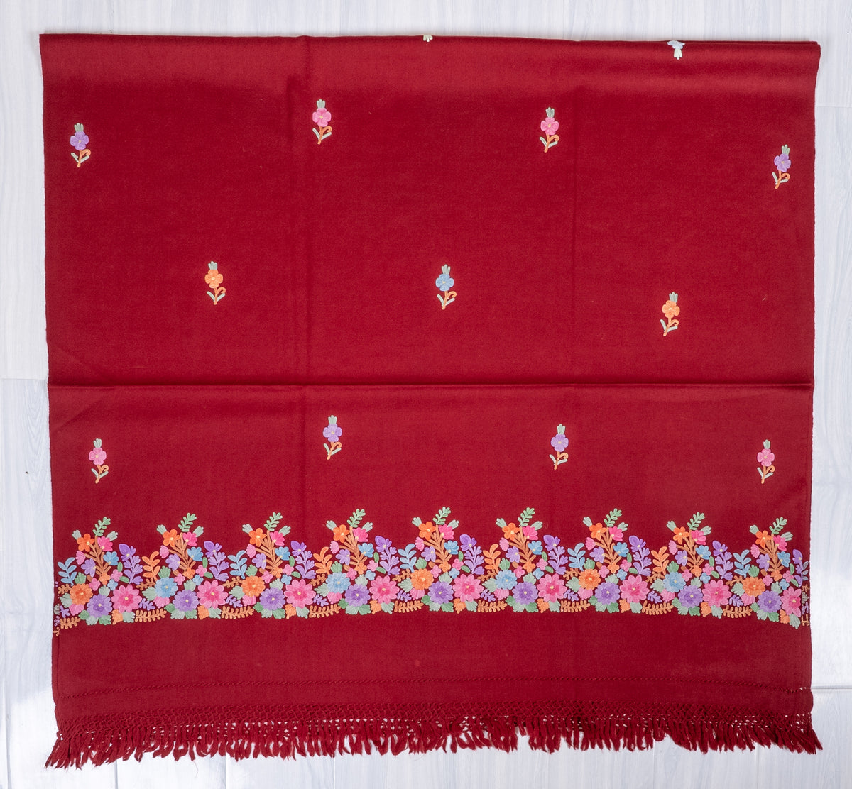 Maroon shawl laid flat, with scattered pastel Aari flower sprigs and a multicoloured floral border above knotted red fringe.