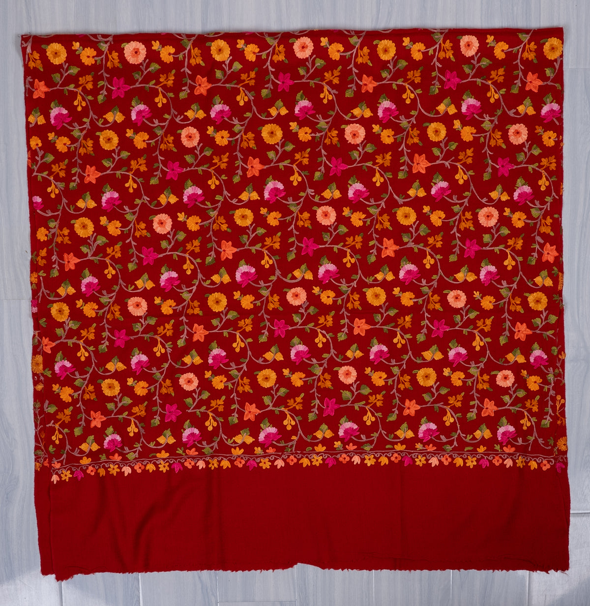 Crimson shawl spread flat, with colourful Aari floral vines across the field and a narrow floral border above the plain end