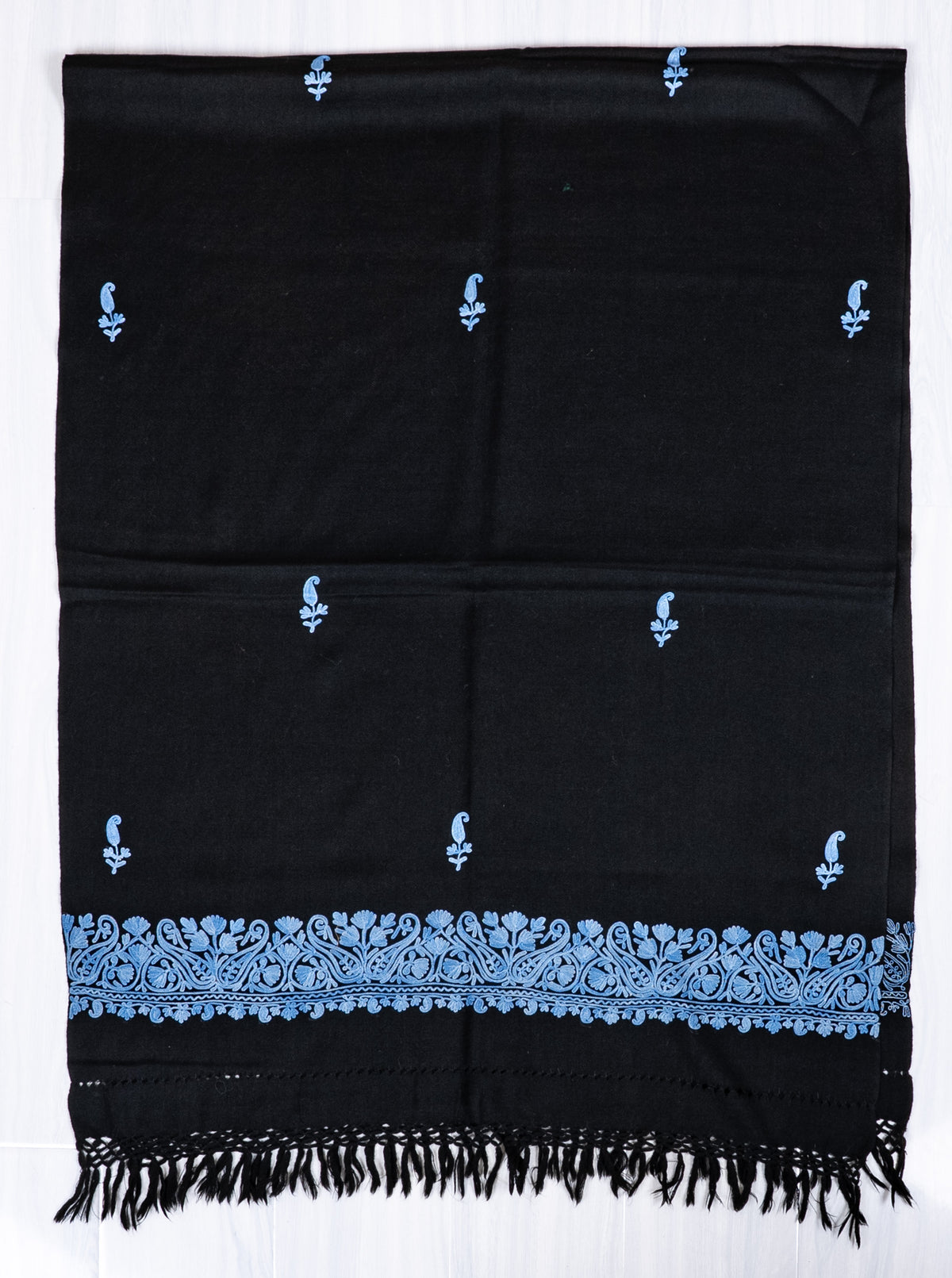 Black shawl laid flat in a folded section, showing blue Aari paisley sprigs, a floral end border and black knotted fringe