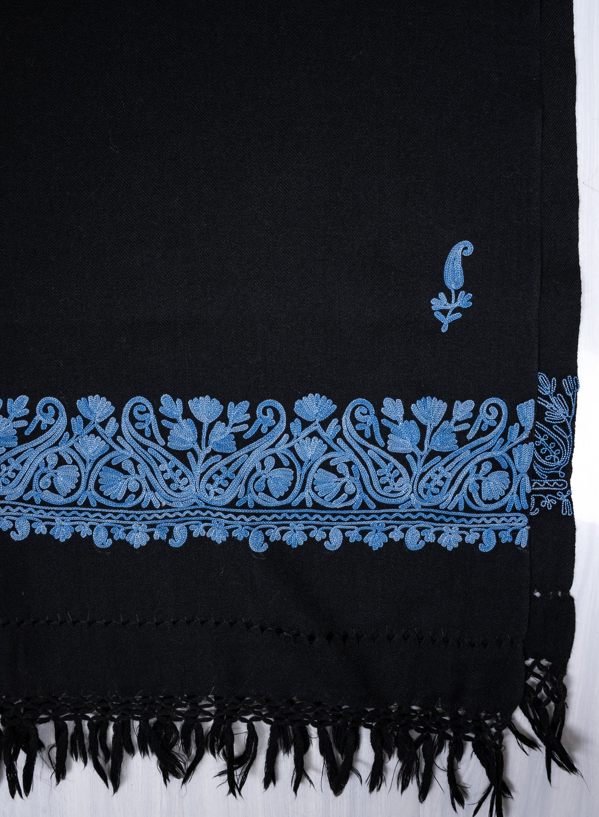 Flat end detail of the black shawl, with a blue Aari paisley sprig above an ornate blue border and black fringe