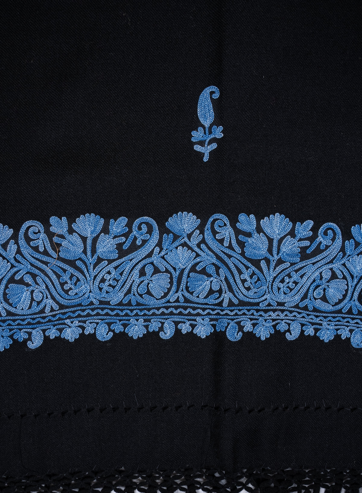 Flat close-up of a blue Aari paisley sprig above the black shawl’s ornate blue floral border