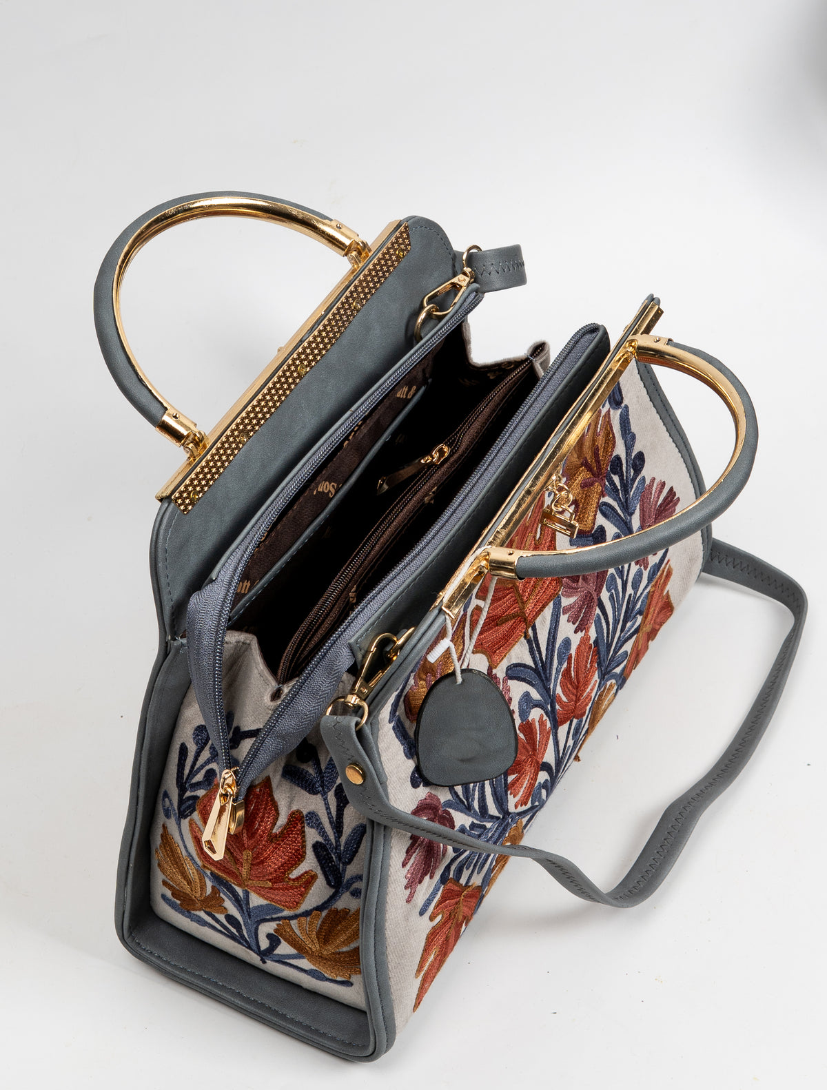 Top view of the open beige handbag, showing a divided brown-lined interior, gold-toned frame and grey strap