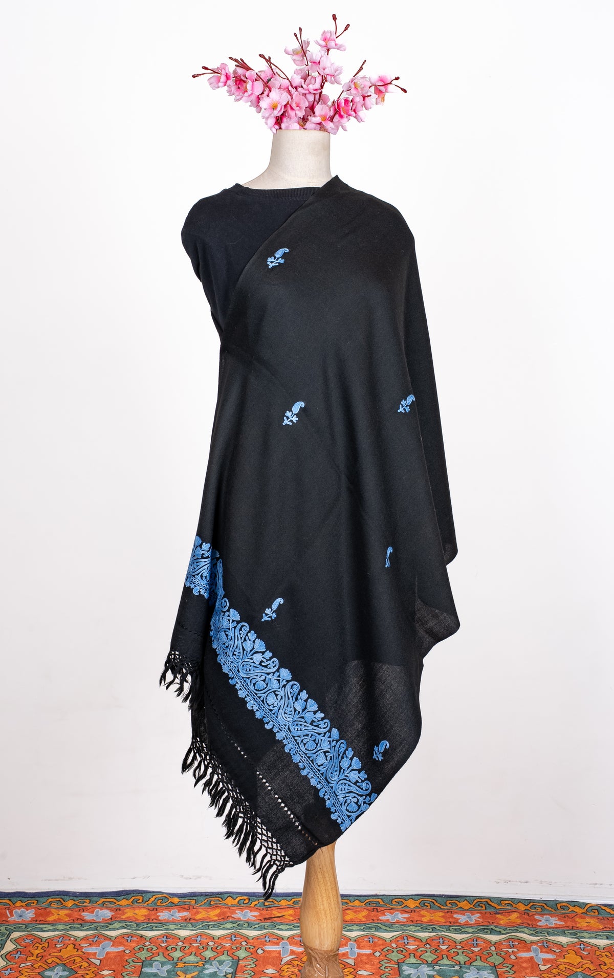 Full draped view of the black shawl on a mannequin, with scattered blue Aari paisley sprigs and a broad floral end border