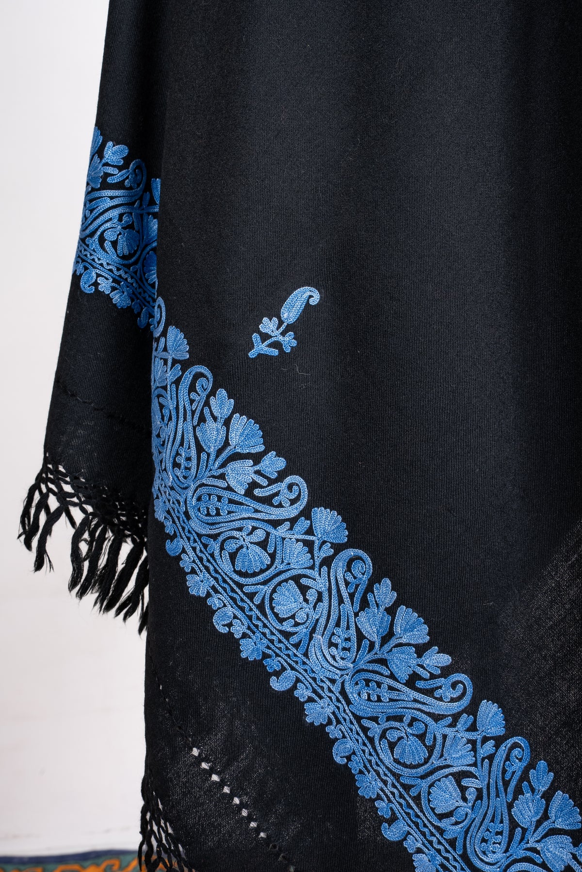 Draped end detail of the black shawl, with blue Aari paisley sprigs, an ornate floral border and black knotted fringe