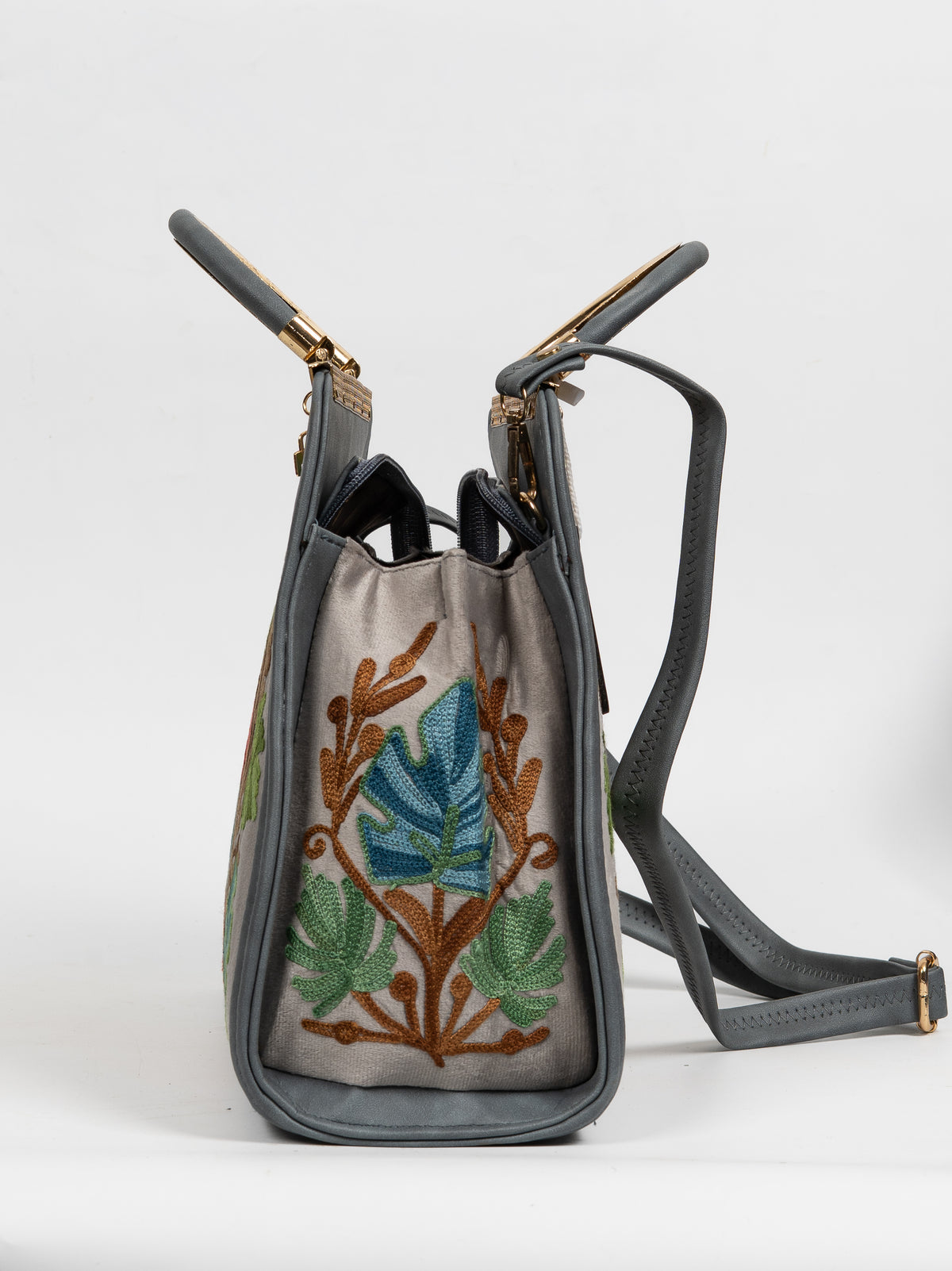 Side view of a grey handbag with a teal and green Aari leaf panel, opened handles and an attached shoulder strap