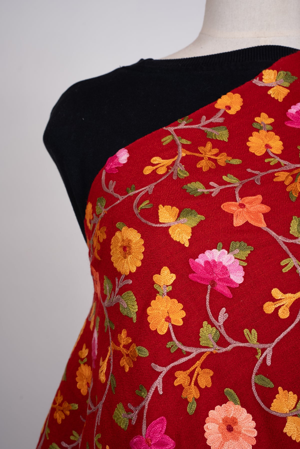 Shoulder close-up of the crimson shawl, showing pink and orange Aari flowers, green leaves and pale curling stems