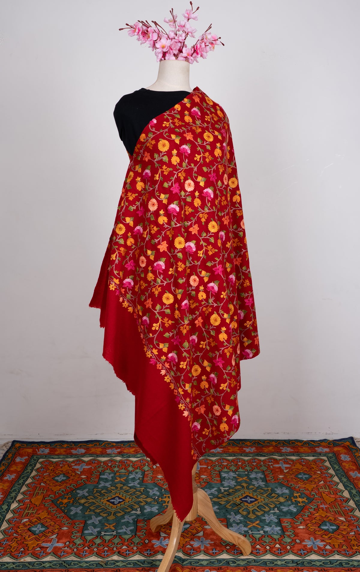 Full view of the crimson shawl on a mannequin, covered with pink and orange Aari flowers above a plain red end
