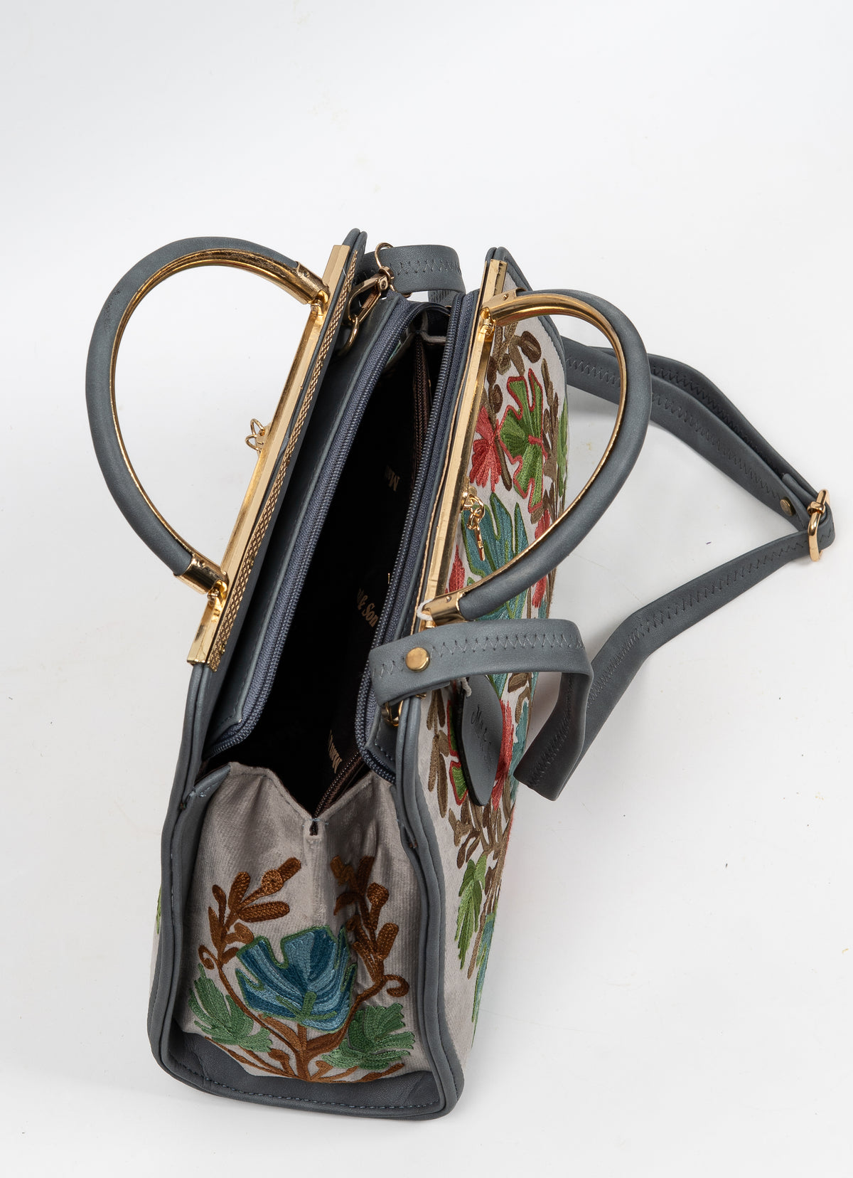 Angled top view of an open grey Aari handbag showing its dark interior, gold-toned frame and handles folded outward