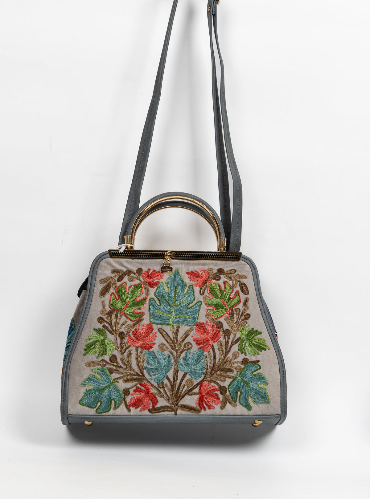 Grey handbag hanging from a long shoulder strap, with teal and green Aari leaves, coral flowers and gold-toned handles