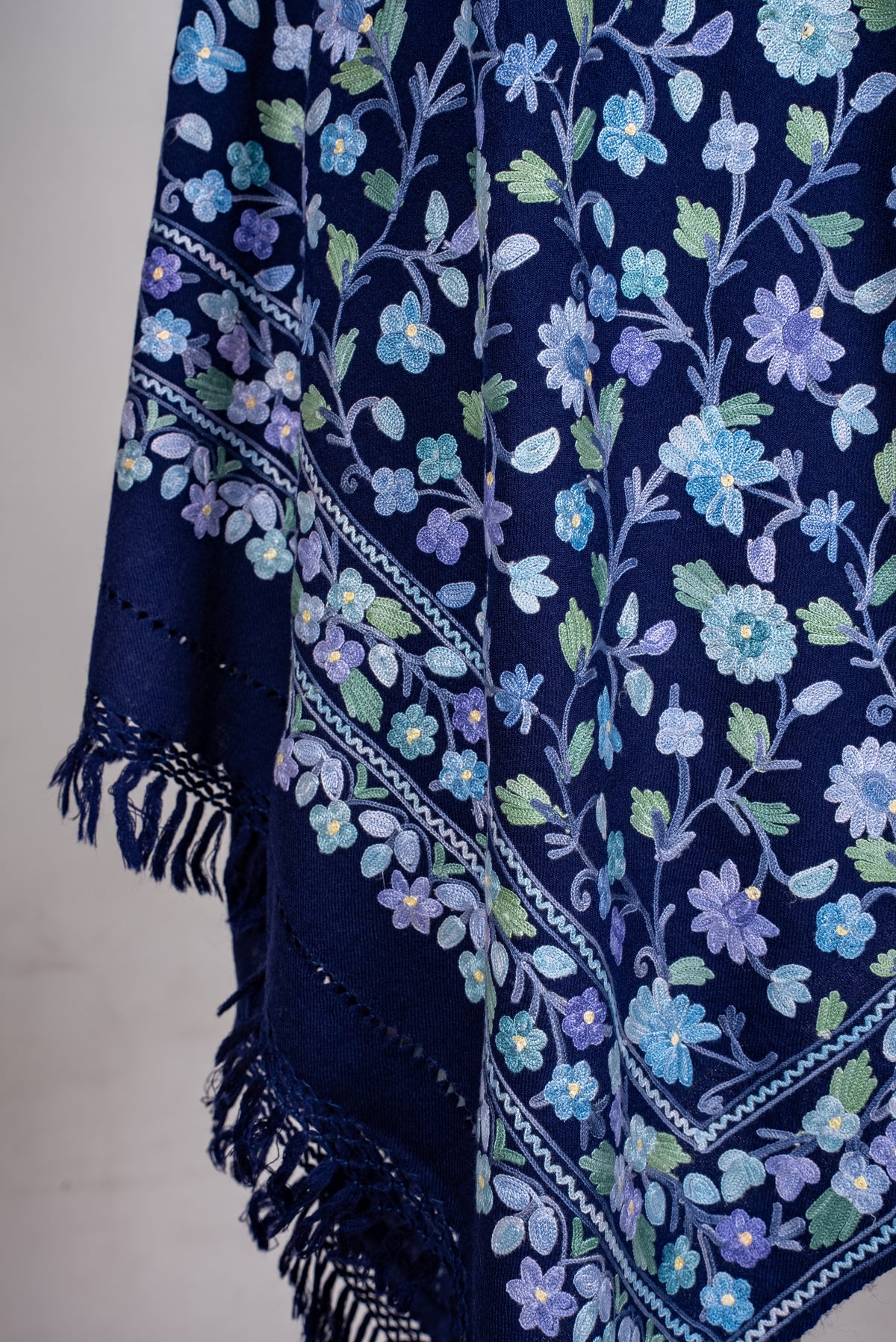 Lower draped corner of the sapphire shawl, showing pale Aari flowers above layered floral borders and dark blue fringe