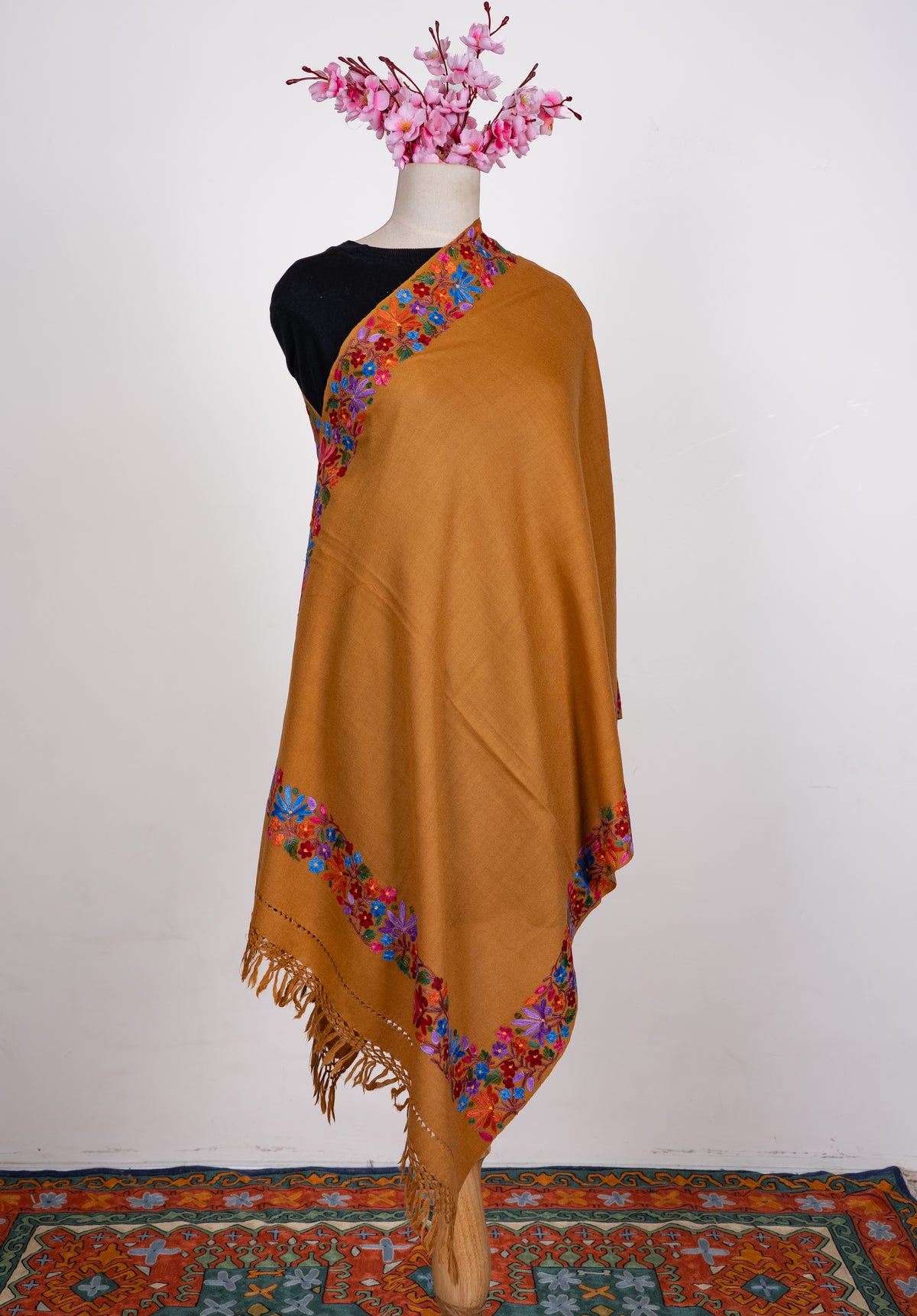 Full view of the mustard shawl on a mannequin, with a plain centre, colourful Aari floral borders and matching fringe