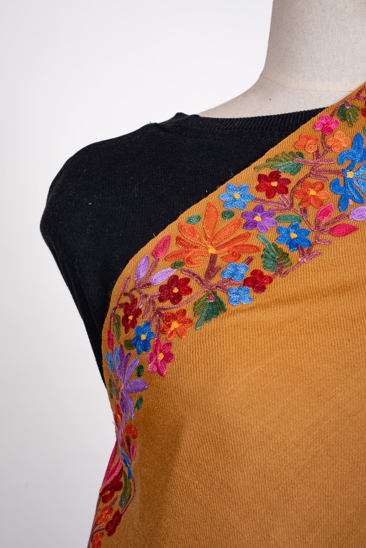 Shoulder close-up of the mustard shawl, showing blue, pink, orange and red Aari flowers with green leaves along the border