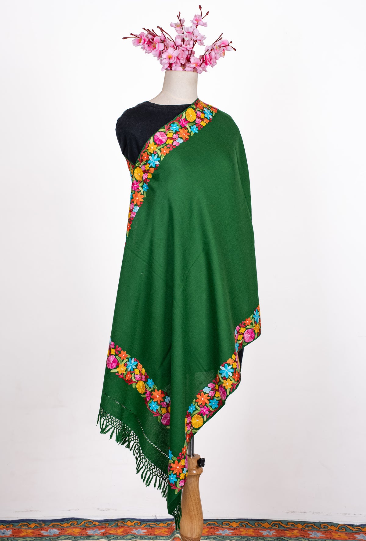 Full view of the forest-green shawl on a mannequin, with a plain centre, colourful Aari borders and matching knotted fringe