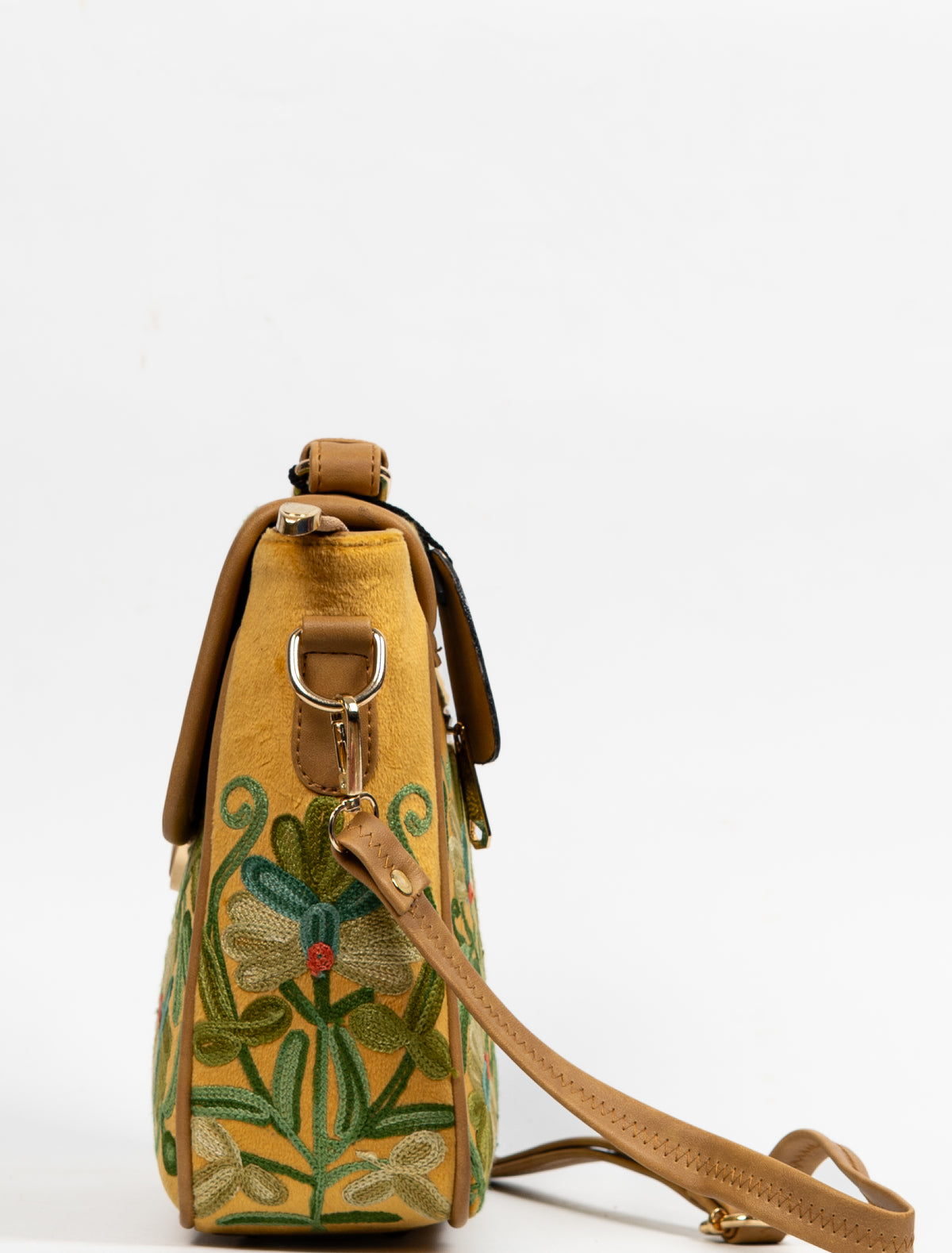 Side view of the mustard bag with floral embroidery across the gusset and a tan strap clipped to the metal ring.