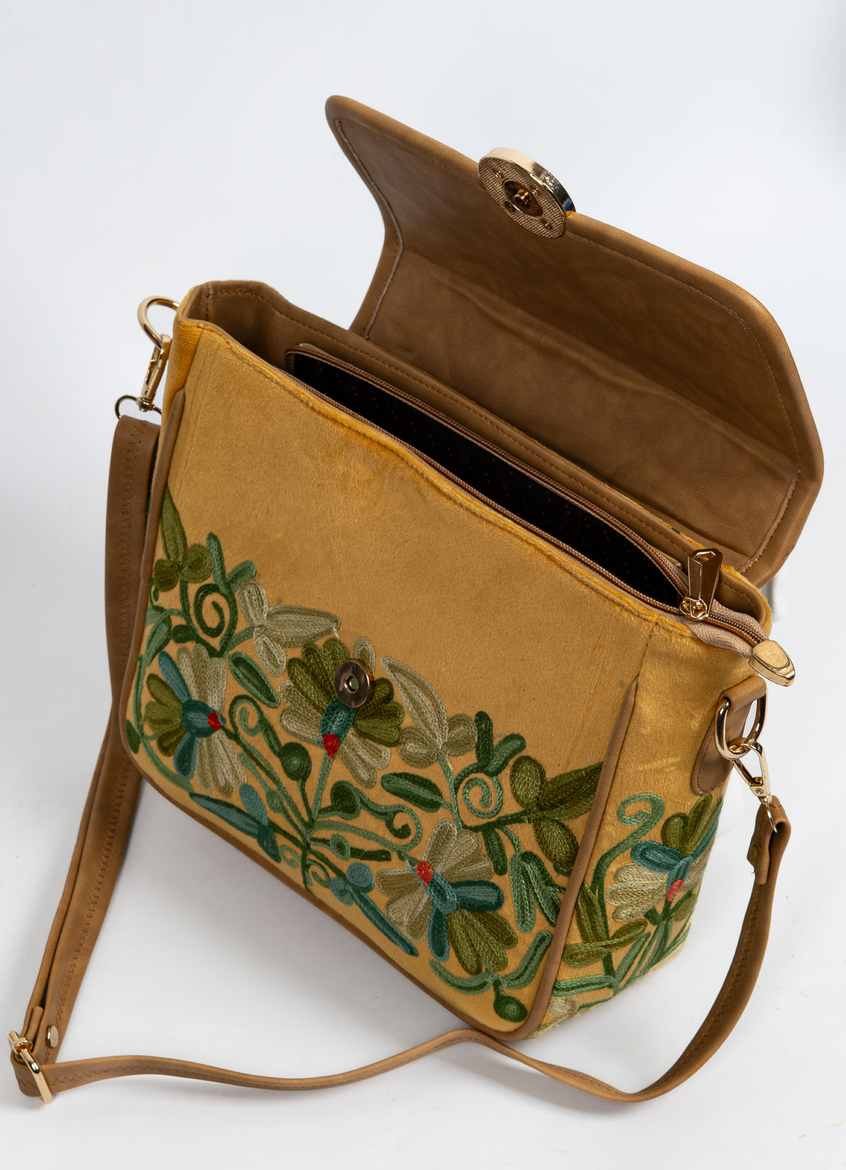 Open mustard bag with the flap lifted, showing a zippered interior opening, tan lining and floral embroidery beneath the flap.