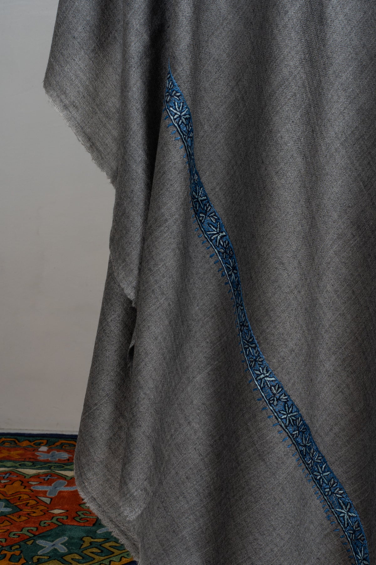 Draped folds of a grey Merino wool shawl with a narrow blue Sozni floral border.