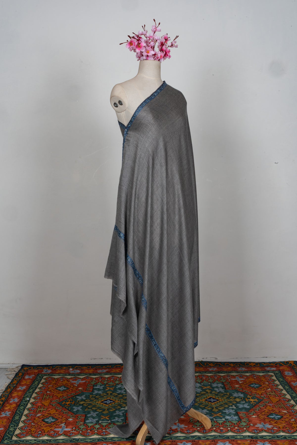 Full-length view of a grey Merino wool shawl draped over one shoulder of a mannequin with narrow blue Sozni borders.