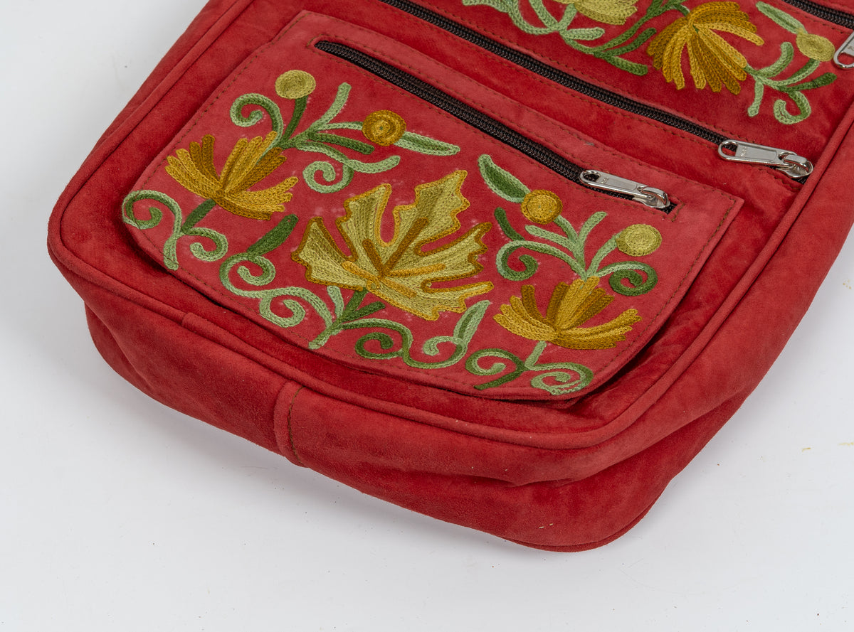 Close-up of the red bag’s lower front pocket with yellow flowers, green curling stems and silver-toned zipper pulls.