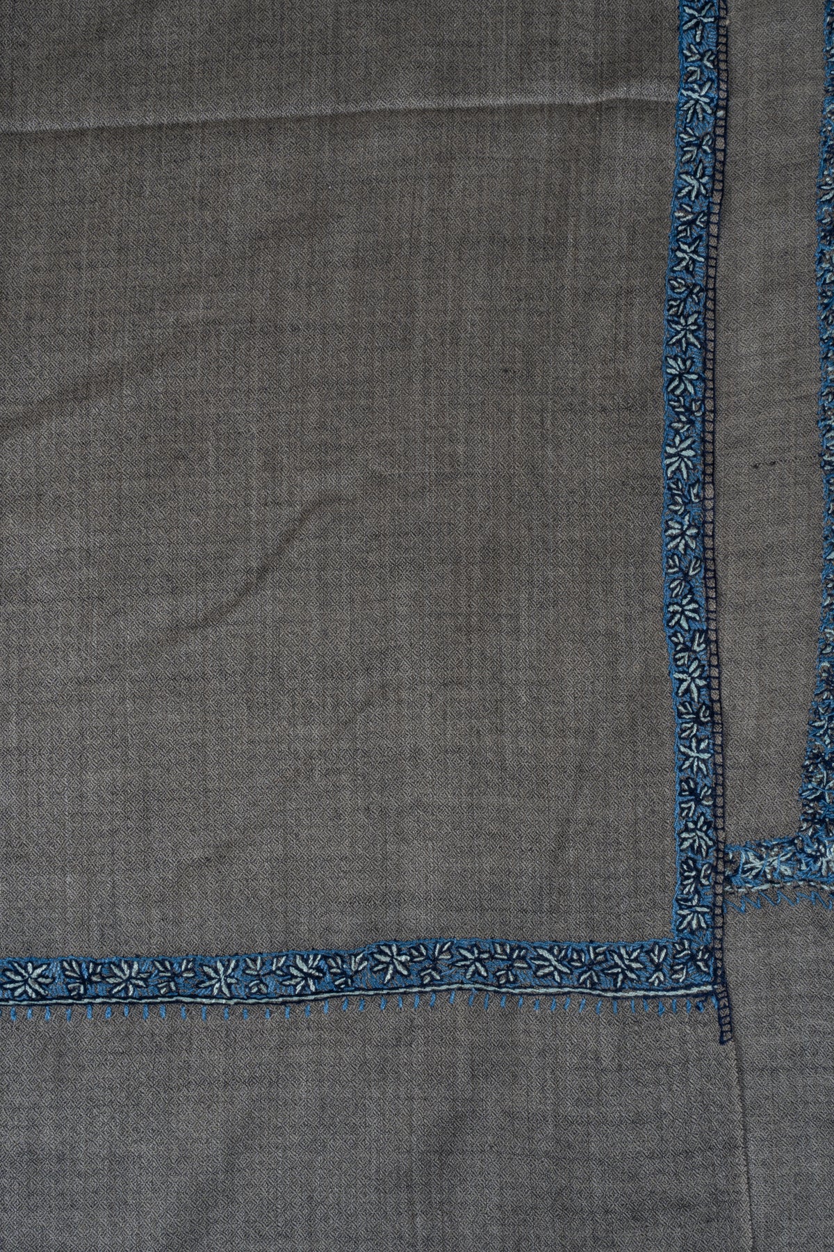 Corner of a grey Merino wool shawl with narrow blue Sozni floral borders.