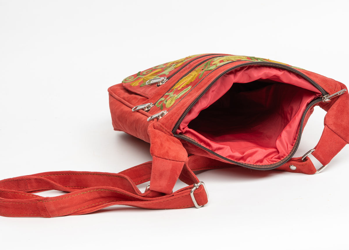 Red crossbody bag laid on its side with the main zipper open, revealing the red lining and adjustable strap.
