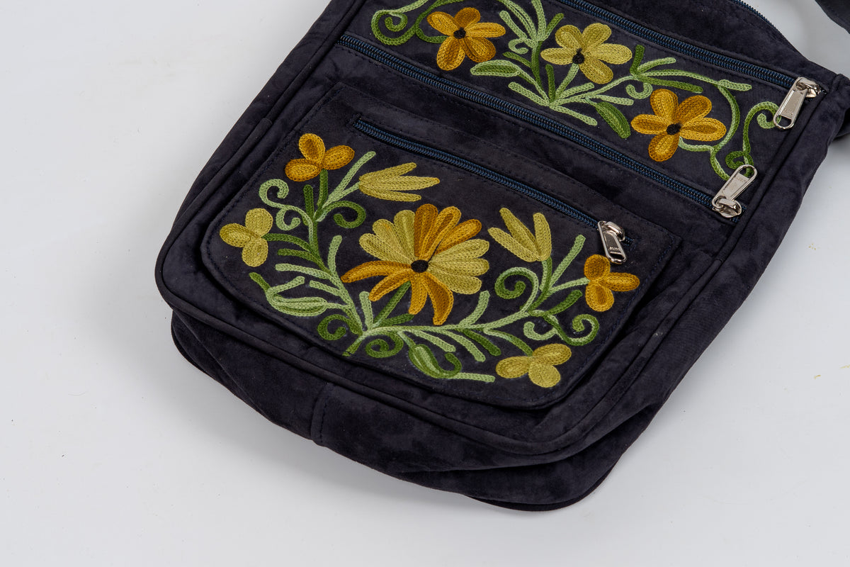 Close-up of the black front pockets with yellow floral embroidery, green curling stems and silver-coloured zipper pulls.