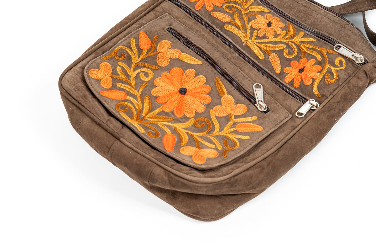 Close-up of the bag front pockets with orange and golden floral embroidery, brown piping and silver-coloured zipper pulls.