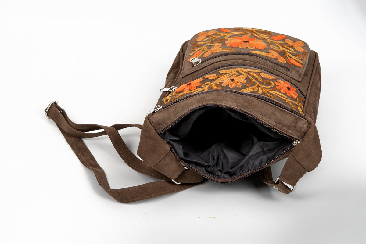 Open top view of the brown messenger bag showing its black lining, zippered opening and embroidered front pockets.
