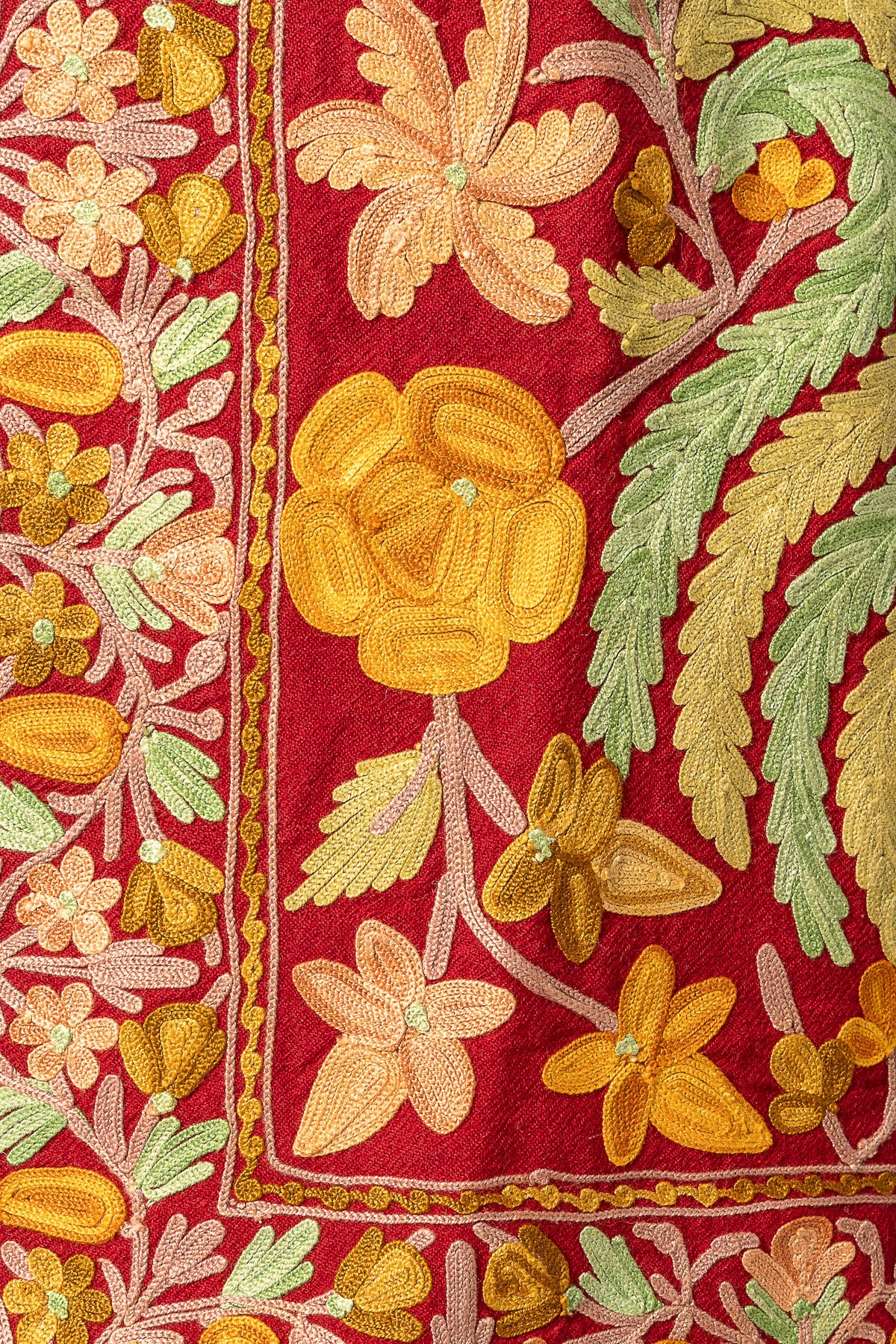 Close-up of a yellow embroidered flower and pale green leaves beside the maroon jacket's floral border