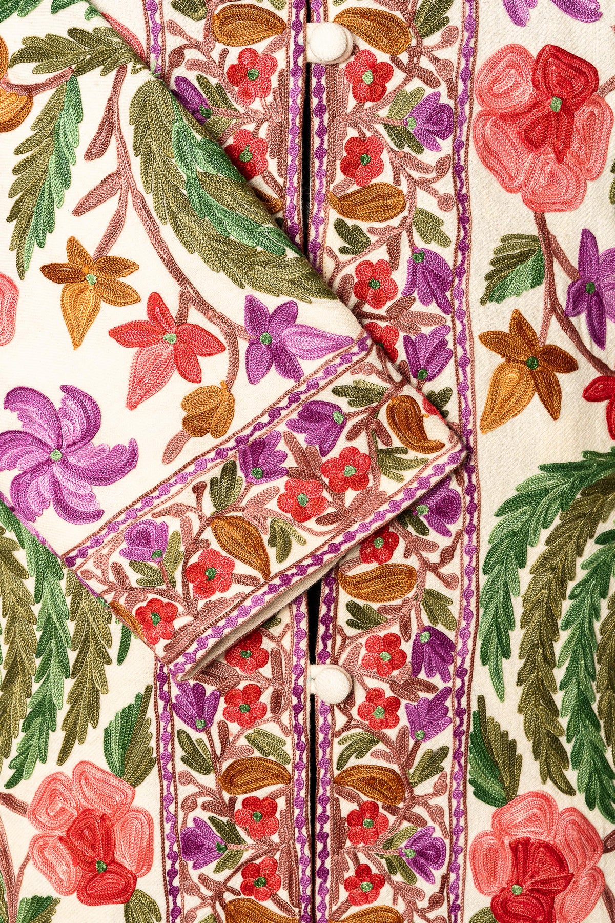 Close-up of the white jacket's embroidered cuff and front border beside white covered buttons