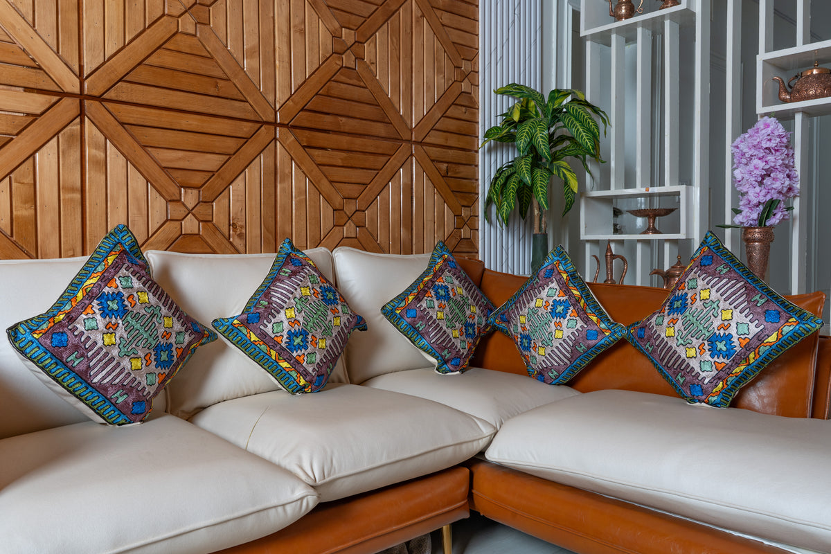 Five matching embroidered cotton cushions arranged across a cream corner sofa, with bright geometric motifs