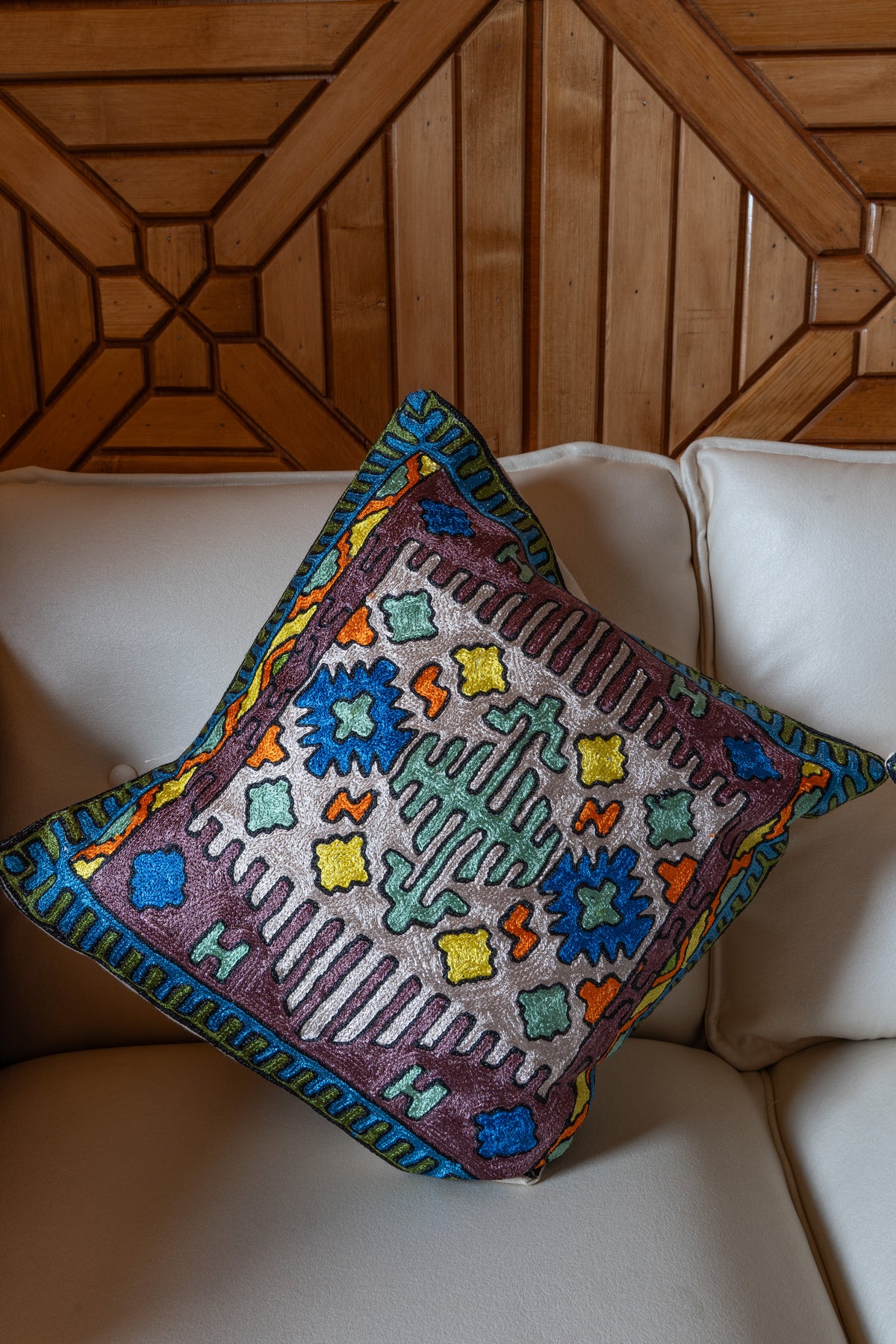 Cotton cushion on a cream sofa, showing a mint central geometric motif, blue rosettes and a plum border