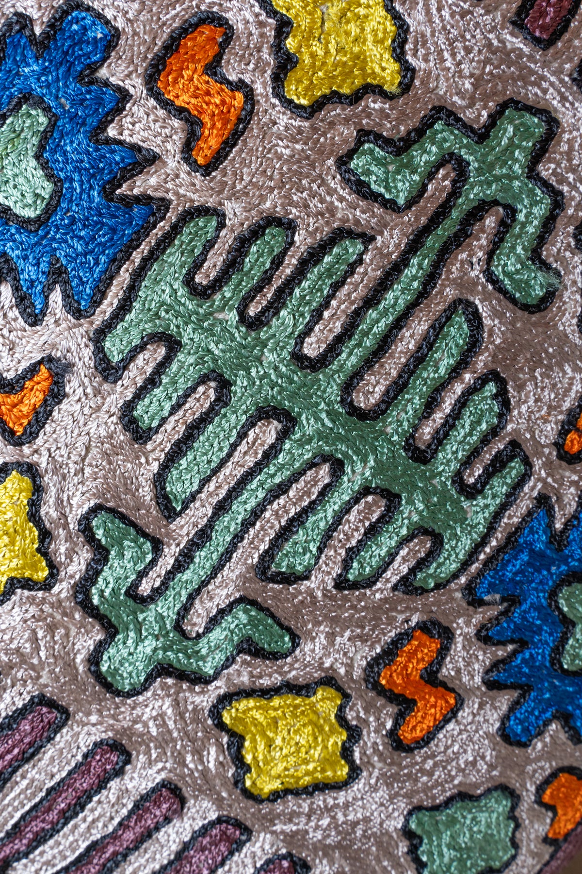 Close-up of textured mint, blue, yellow and orange geometric embroidery with dark outlines on a cotton cushion cover