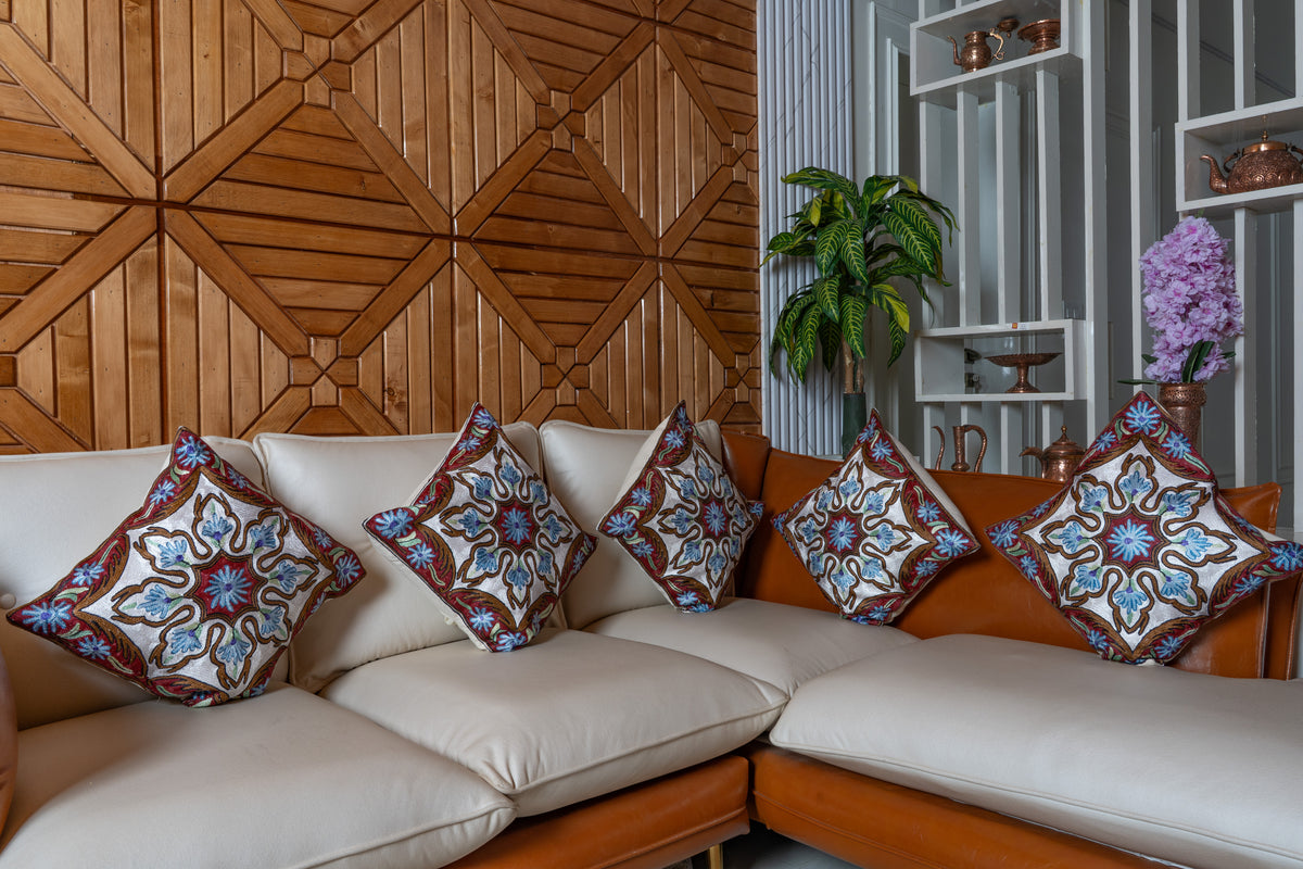 Five matching cotton cushions across a cream corner sofa, with blue and ivory floral embroidery and deep red borders